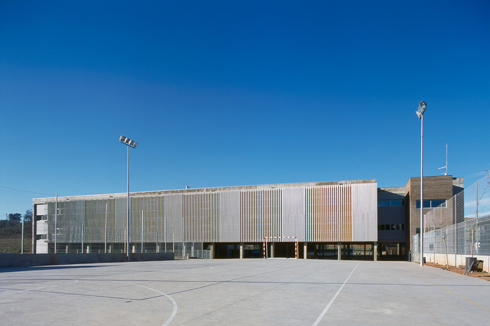 Exterior view showcasing a spacious outdoor sports court and the building's facade with vertical metal slats and concrete columns.