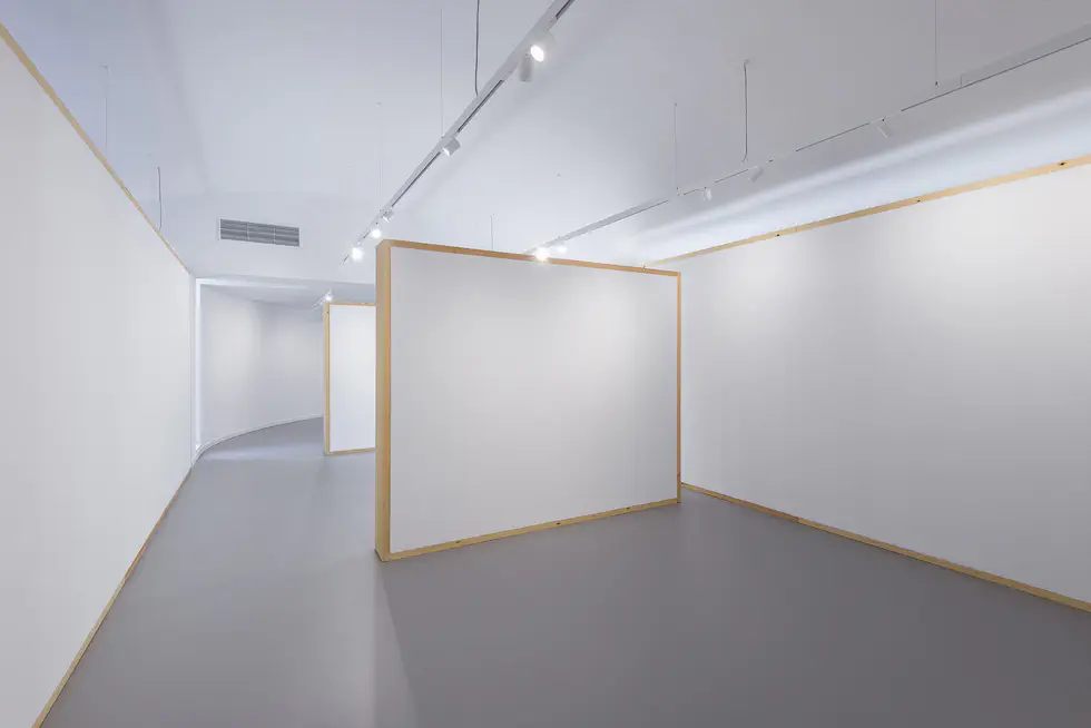 Interior view featuring modular white walls with wooden frames, a curved passageway in the background, and overhead track lighting.
