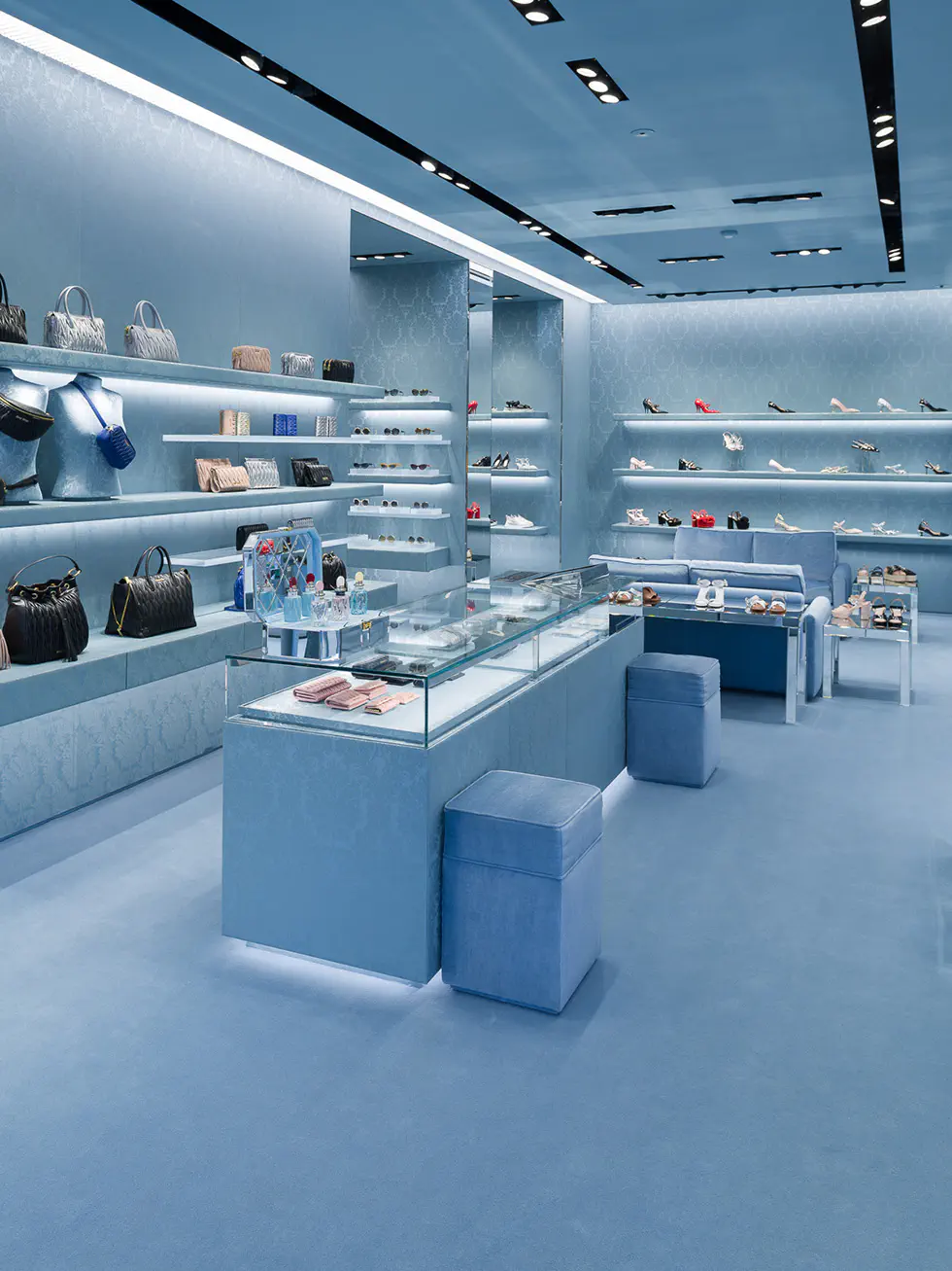 A chic Miu Miu store interior, all in blue, showcasing sleek display shelves with handbags and shoes, and a glass display counter with accessories.