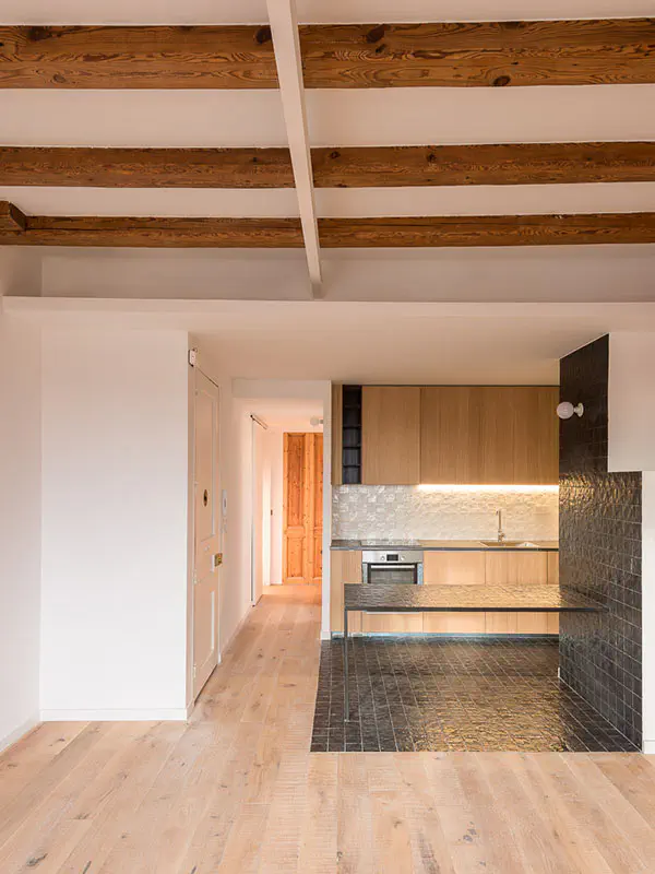 Open kitchen with wooden cabinets, black tiled countertop, and wooden beams on the ceiling.