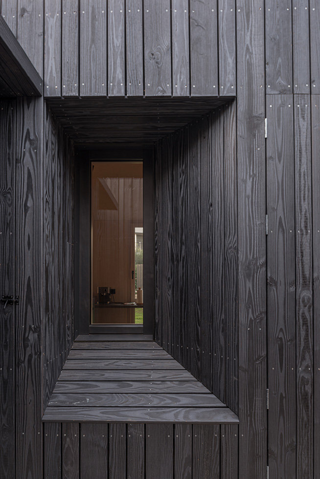 Close-up of a dark wood-clad exterior with a recessed window, showcasing detailed craftsmanship and design.