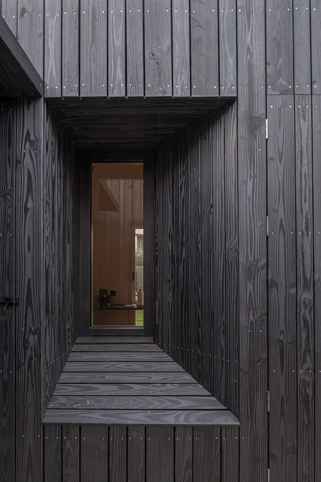 Close-up of a dark wood-clad exterior with a recessed window, showcasing detailed craftsmanship and design.