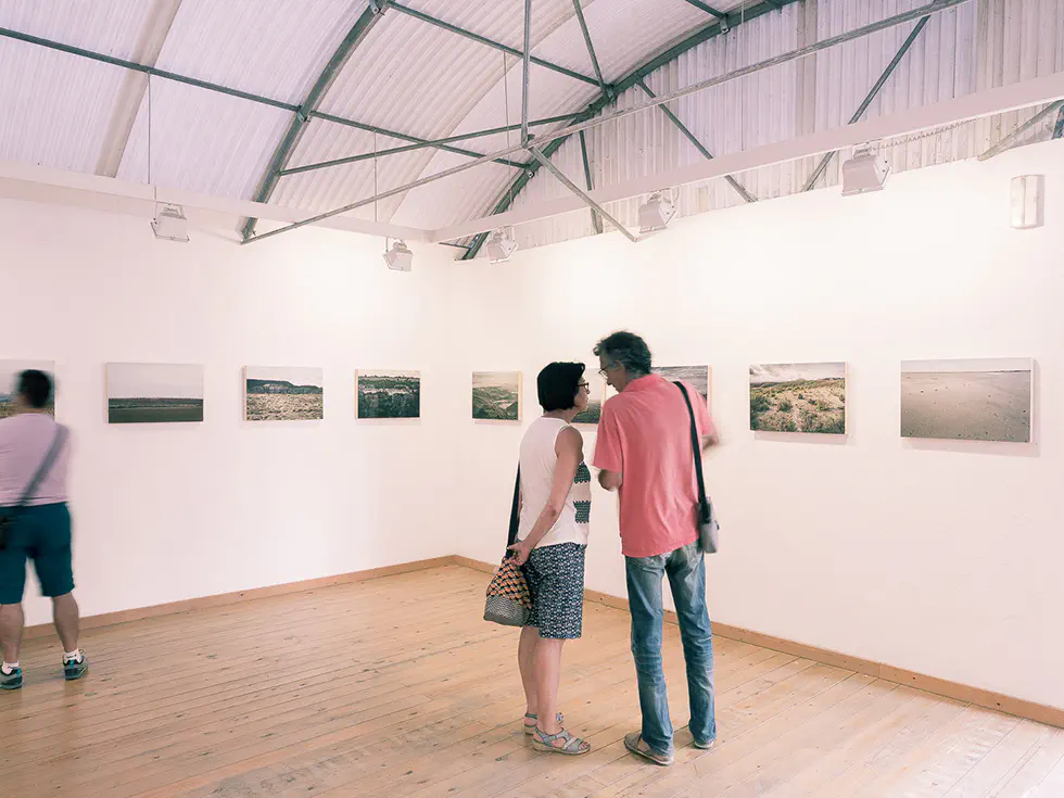 Two people talking in a gallery room with landscape photographs on the wall.