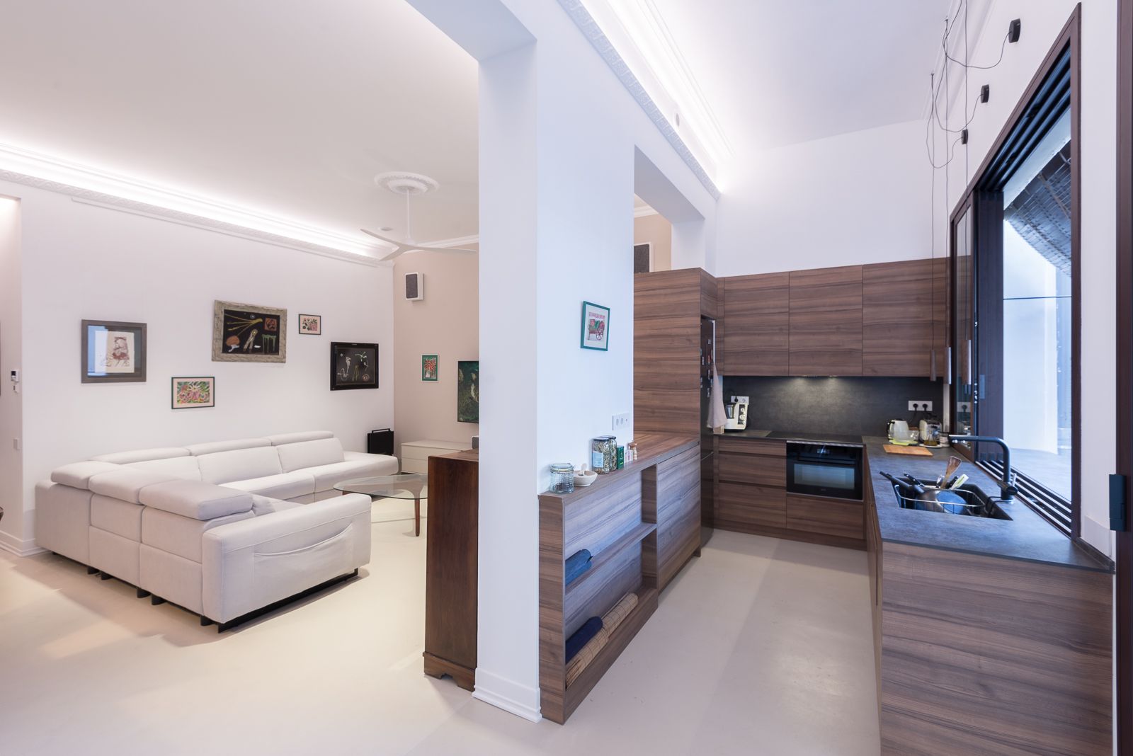 Zona d'estar moderna de concepte obert amb un acollidor sofà seccional blanc, adjacent a una cuina de fusta elegant amb electrodomèstics integrats.
