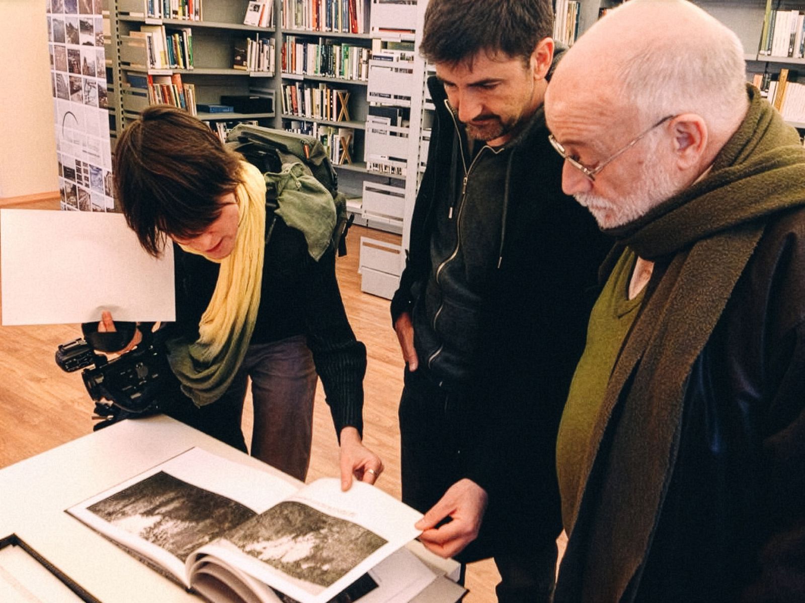 Tres personas mirando un libro abierto con fotografías de paisajes.