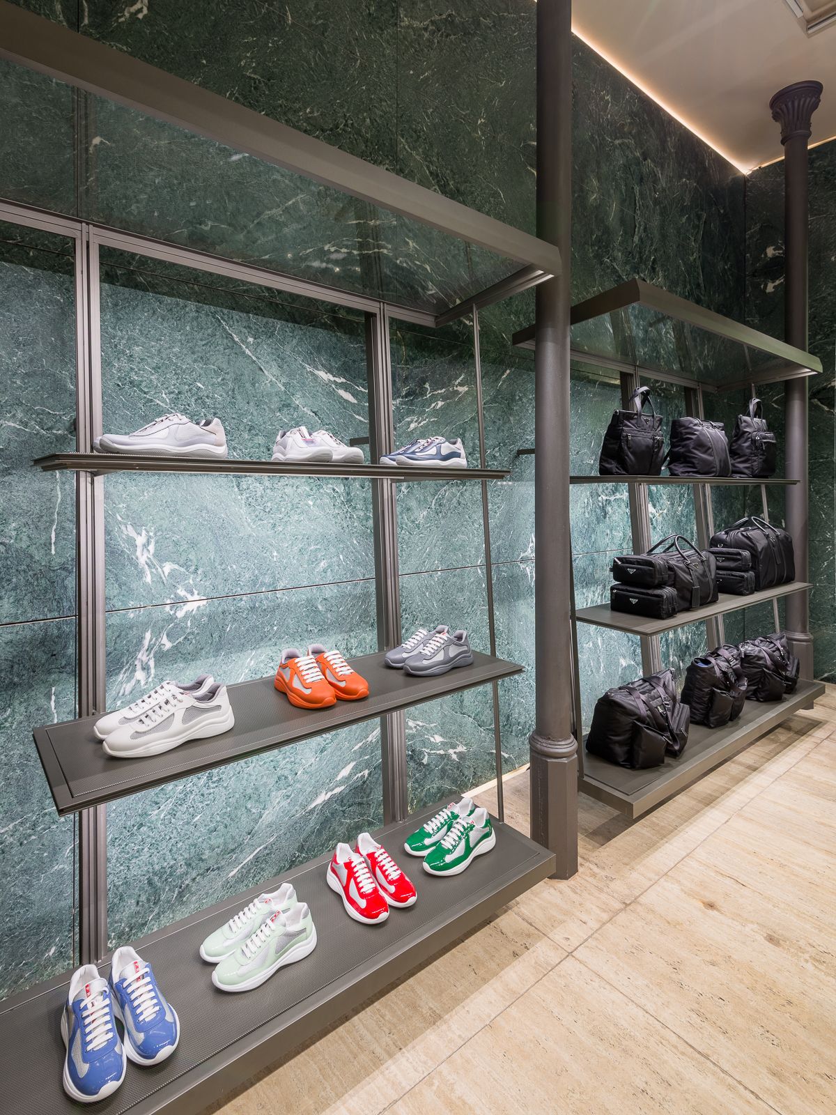 Boutique de luxe Prada amb parets de marbre verd, mostrant sabatilles esportives de dissenyador i bosses negres en prestatges de metall elegant.