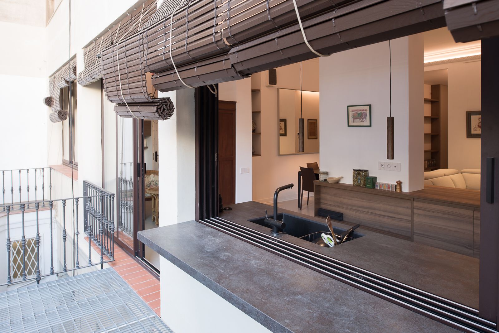 Cuina moderna amb una barra de finestra oberta a la terrassa exterior, amb una encimera elegant i persianes enrotllades.