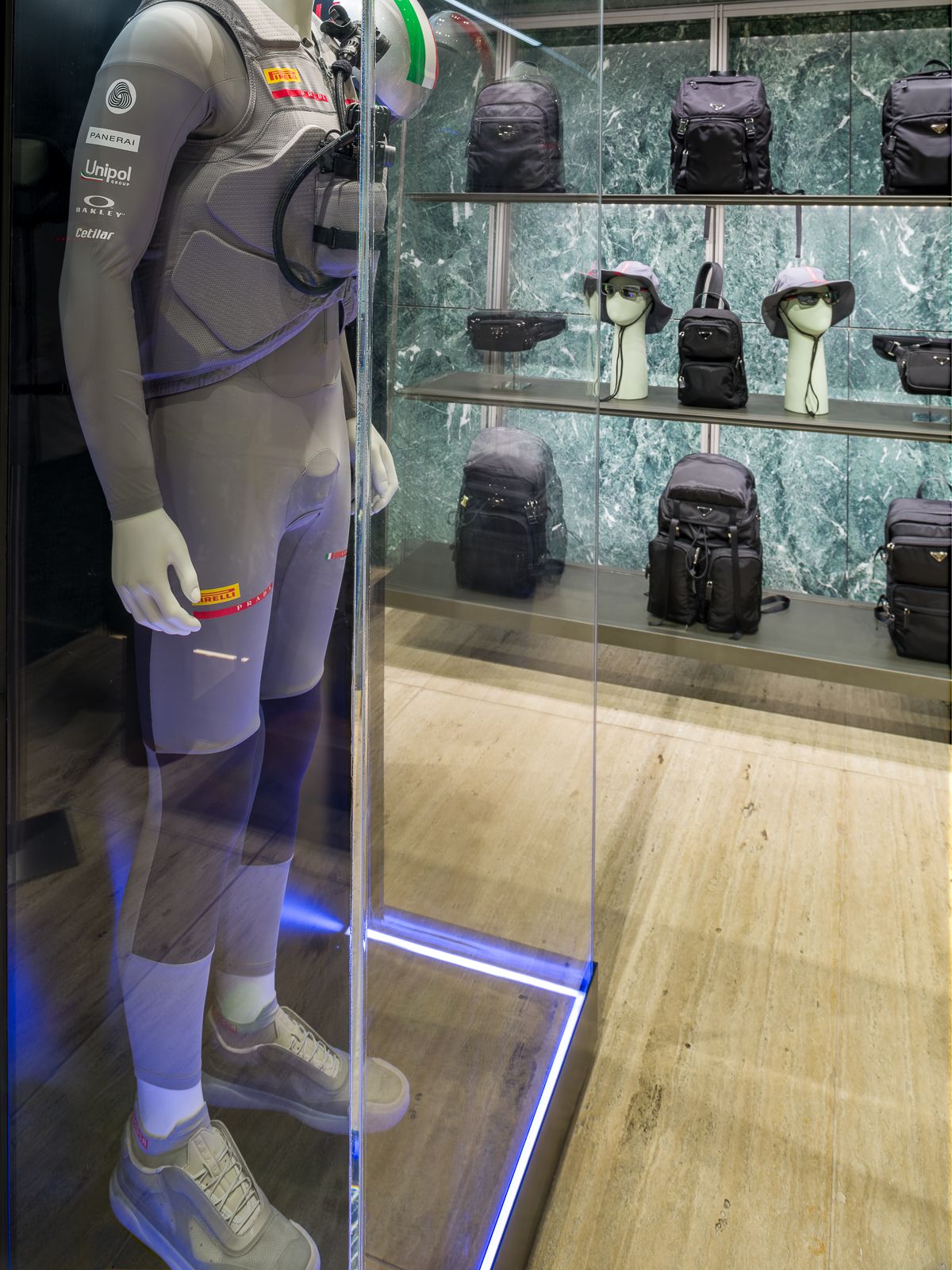 Boutique de luxe Prada amb parets de marbre verd, mostrant un maniquí amb un vestit de rendiment tancat en una vitrina de vidre.