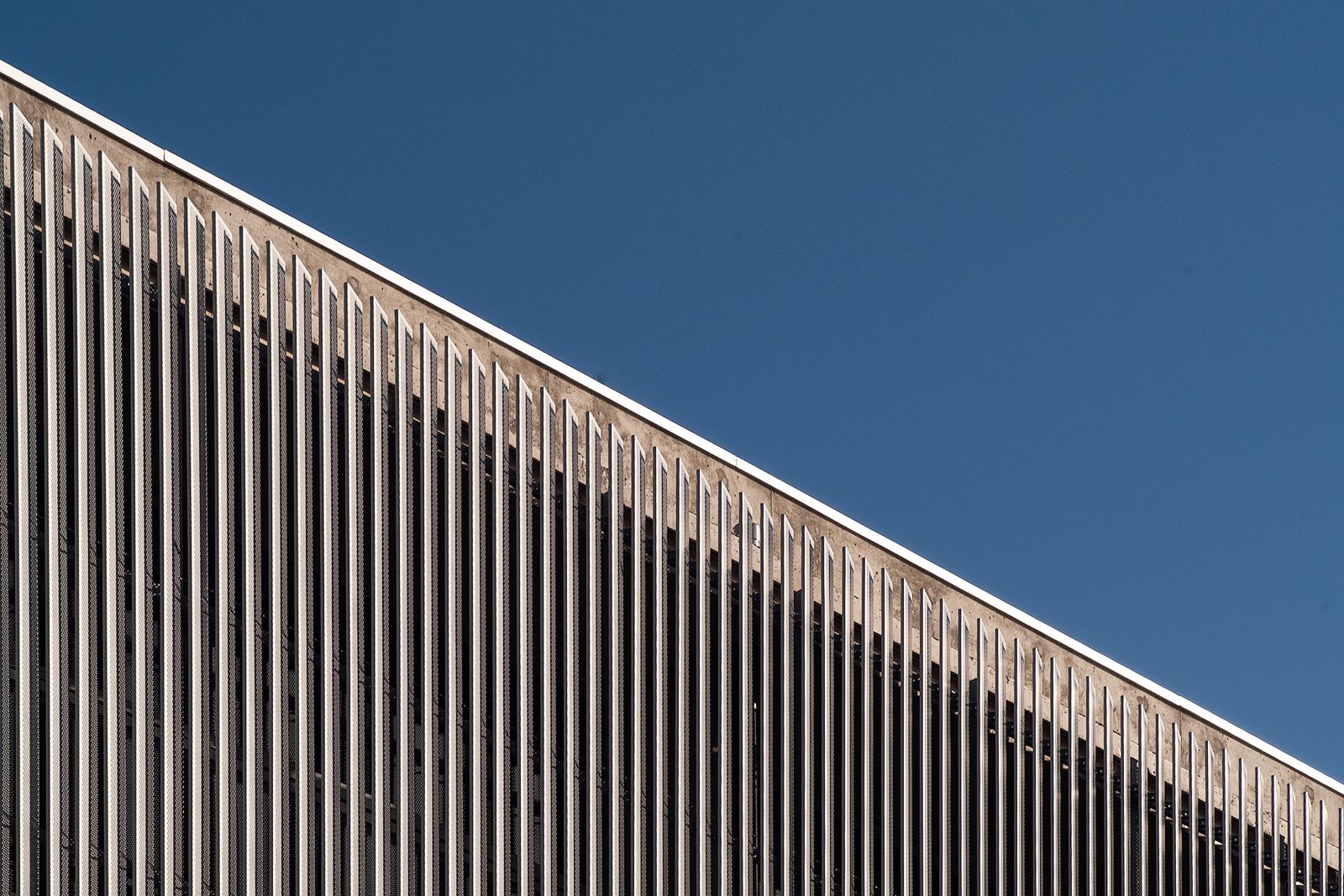 Angled view of Artes High School's facade showcasing the vertical metal slats against a clear blue sky, emphasizing the modern architectural design.