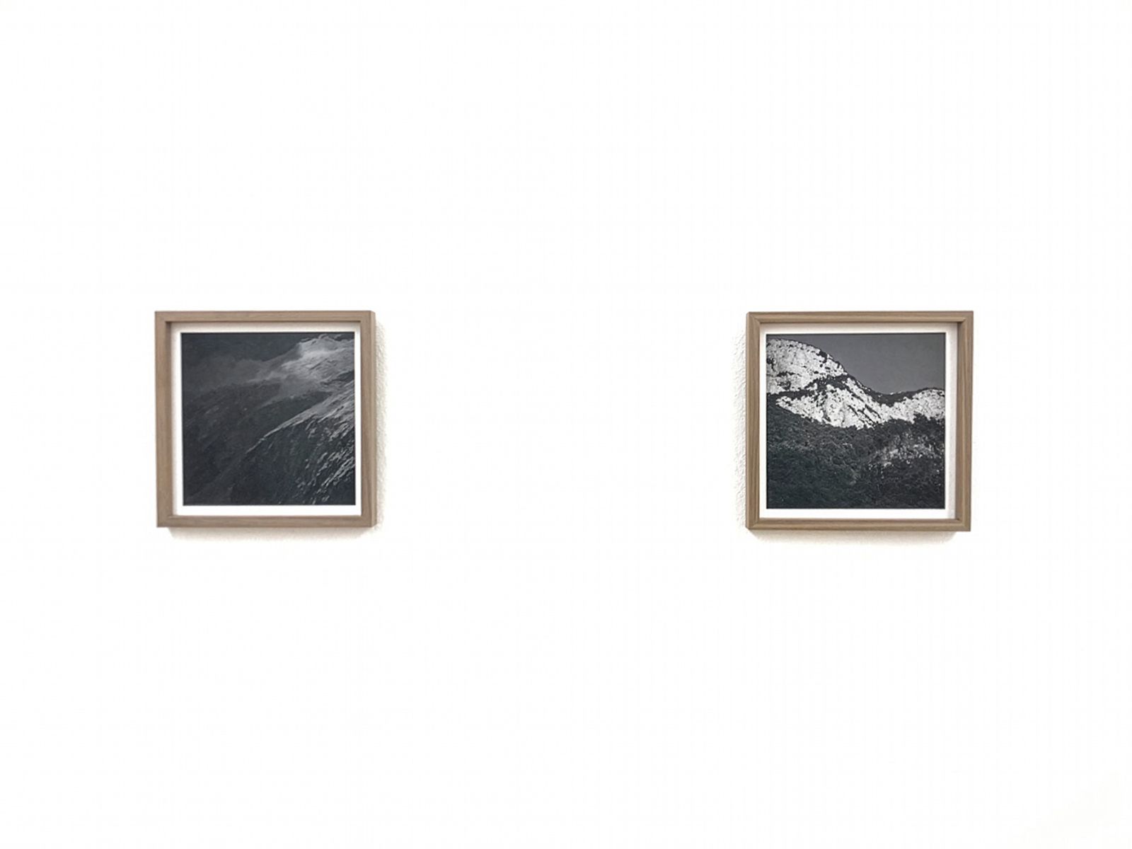 Dos fotografías enmarcadas en blanco y negro de montañas expuestas en una pared blanca en un ambiente de galería minimalista.