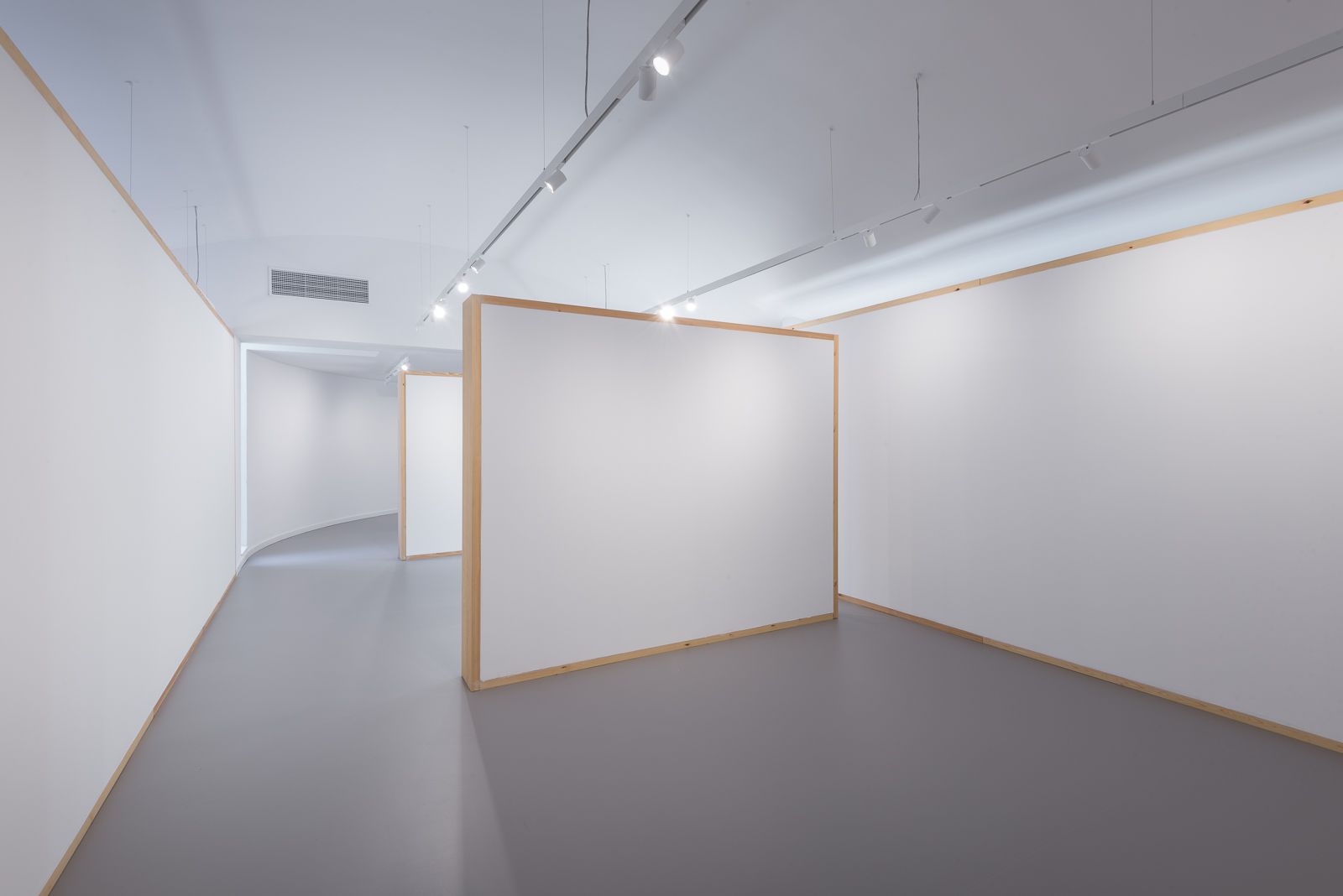 Interior view featuring modular white walls with wooden frames, a curved passageway in the background, and overhead track lighting.