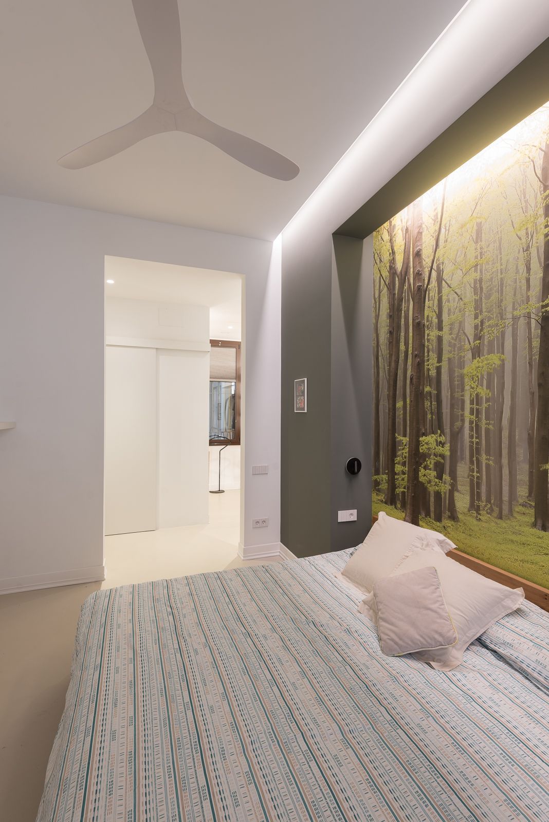 Habitació moderna amb paper pintat amb temàtica de bosc, un ventilador de sostre i il·luminació ambient suau.