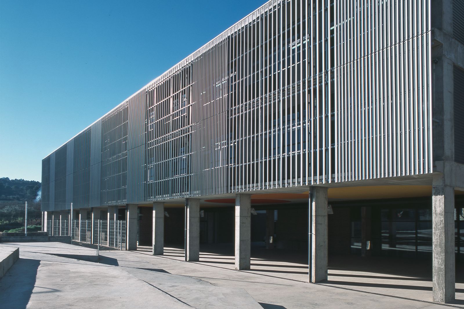 Exterior view featuring a facade with vertical metal slats and concrete columns supporting the structure.