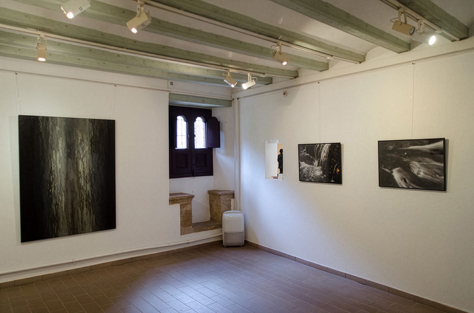 Sala con vigas de techo de madera, suelo de baldosas, fotografías de cascadas en paredes blancas y una pequeña ventana gótica con contraventanas de madera y asiento de ventana medieval de piedra.