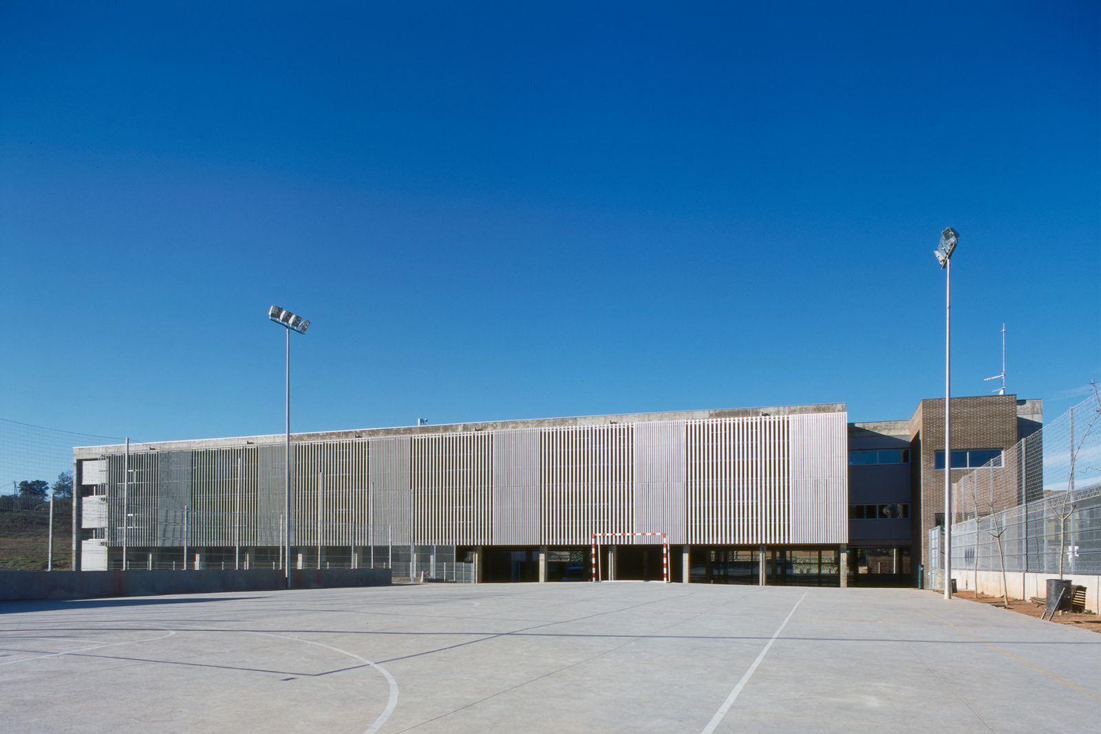 Exterior view showcasing a spacious outdoor sports court and the building's facade with vertical metal slats and concrete columns.