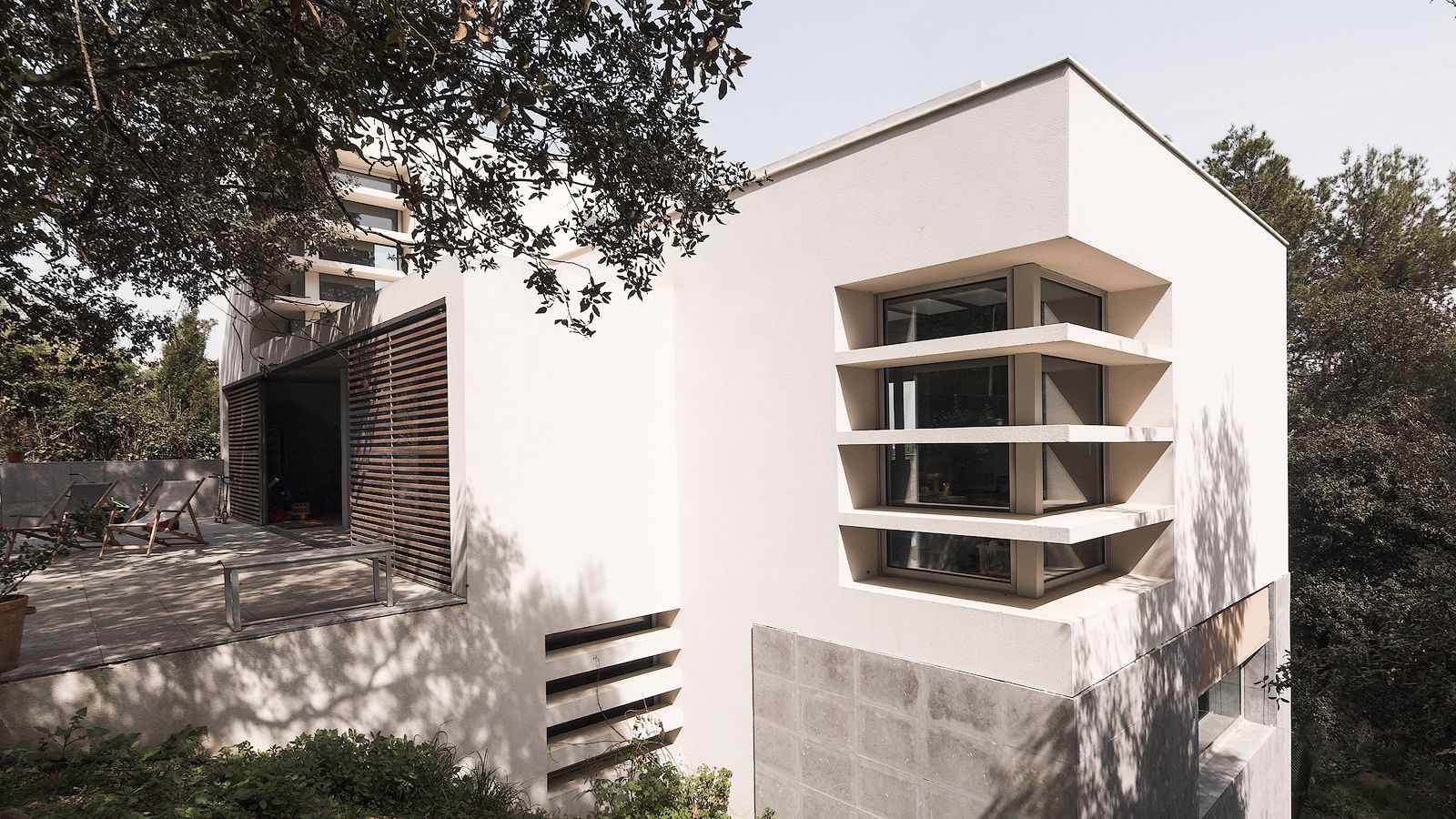 Modern house exterior with large windows and a spacious terrace, surrounded by trees and natural landscape.