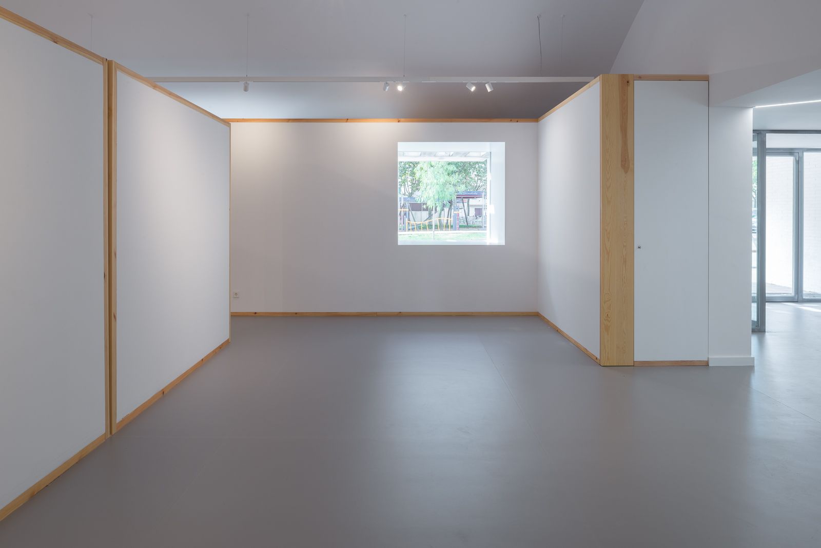 Minimalistic interior with white walls and wooden frames, featuring a single window providing a view of the outdoors.