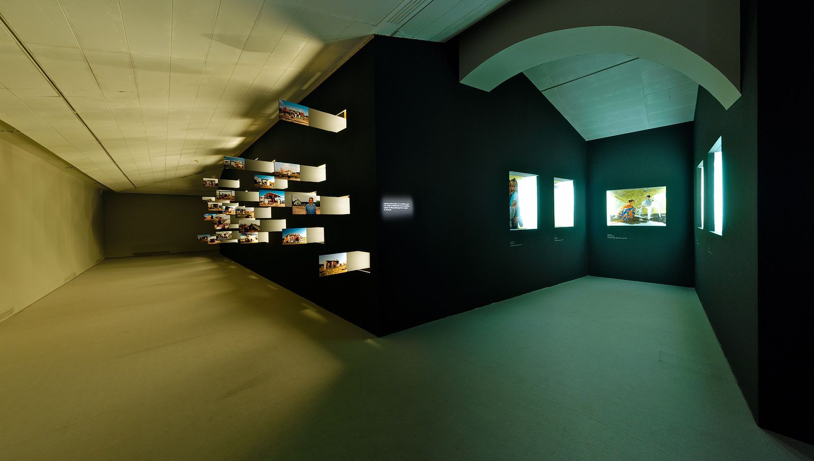 Una sala d'exposició amb poca llum amb múltiples caixes d'exposició i prestatges il·luminats que mostren diverses fotos i objectes a les parets.