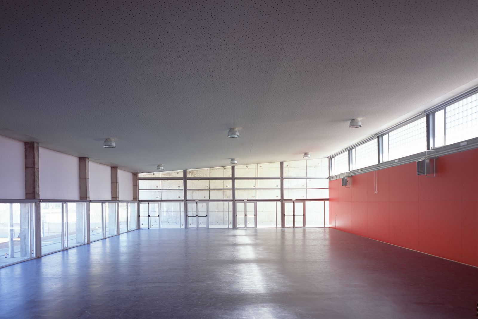 Interior of the gymnasium, featuring a spacious open floor with large windows and a vibrant red accent wall.