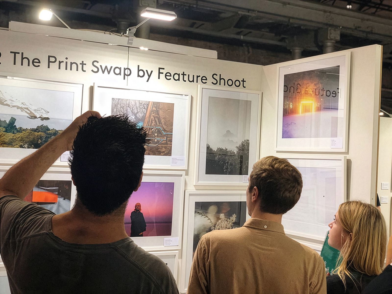 Tres persones veient fotografies emmarcades exposades a l'exposició 'The Print Swap by Feature Shoot'.