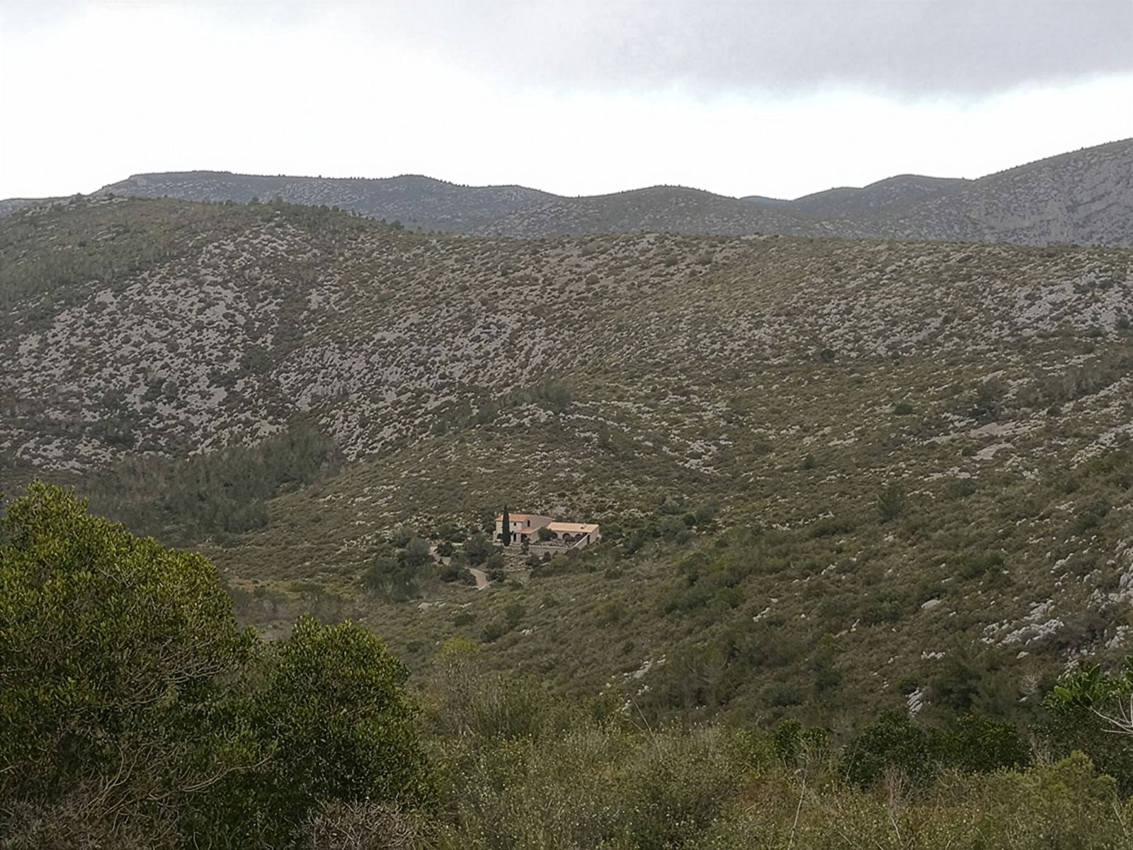 Una casa aislada enclavada en un paisaje montañoso y escarpado con vegetación escasa.