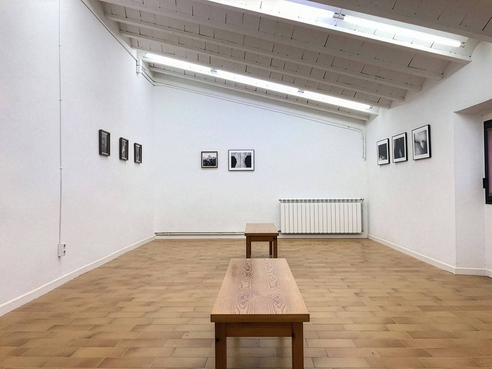 Una sala de galería minimalista con fotografías en blanco y negro en paredes blancas y dos bancos de madera en el centro.