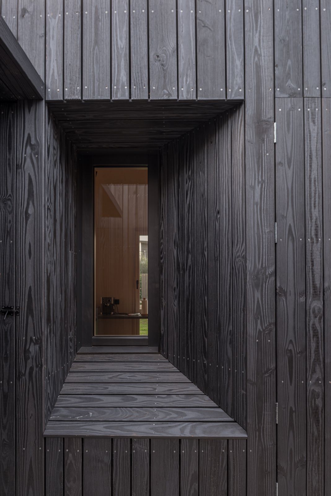 Close-up of a dark wood-clad exterior with a recessed window, showcasing detailed craftsmanship and design.