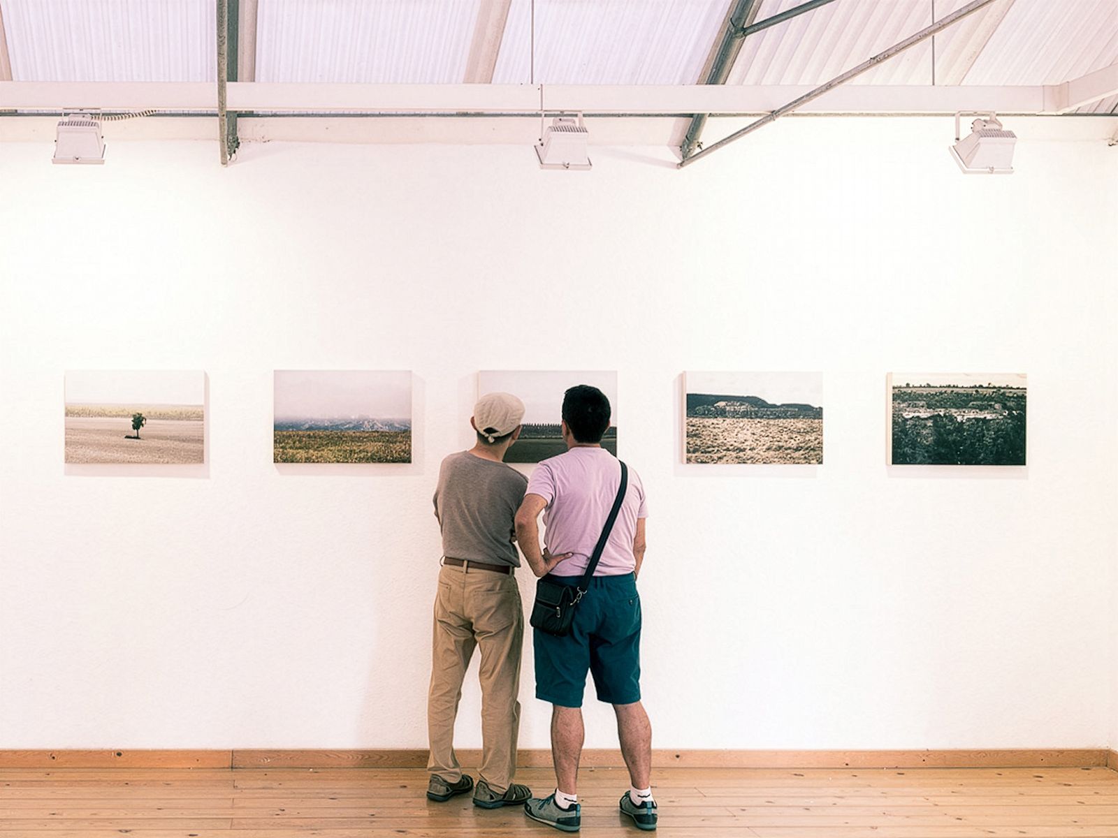 Dos personas viendo de cerca una fotografía en una sala de galería con fotografías de paisajes en la pared.