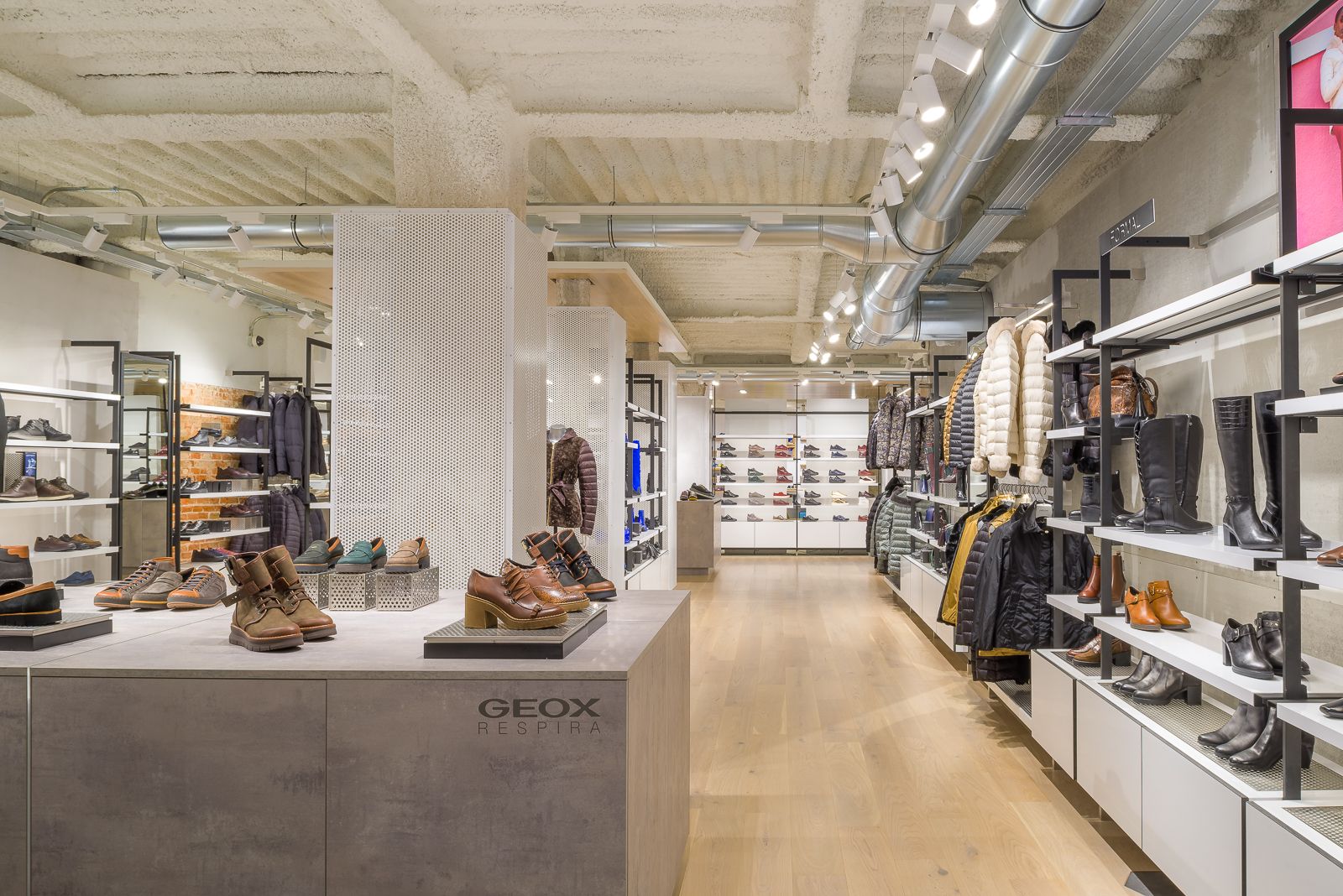 Interior of Geox store displaying a variety of shoes and outerwear, with a modern industrial ceiling design.