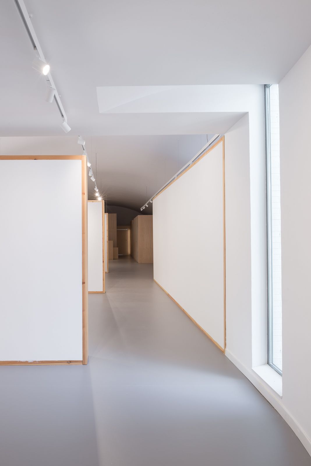 Hallway with minimalist design, featuring white walls, wooden frames, and a large window on the right.