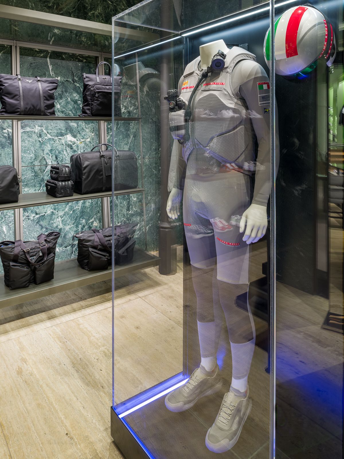 Boutique de luxe Prada amb parets de marbre verd, mostrant un maniquí amb un vestit de rendiment tancat en una vitrina de vidre.