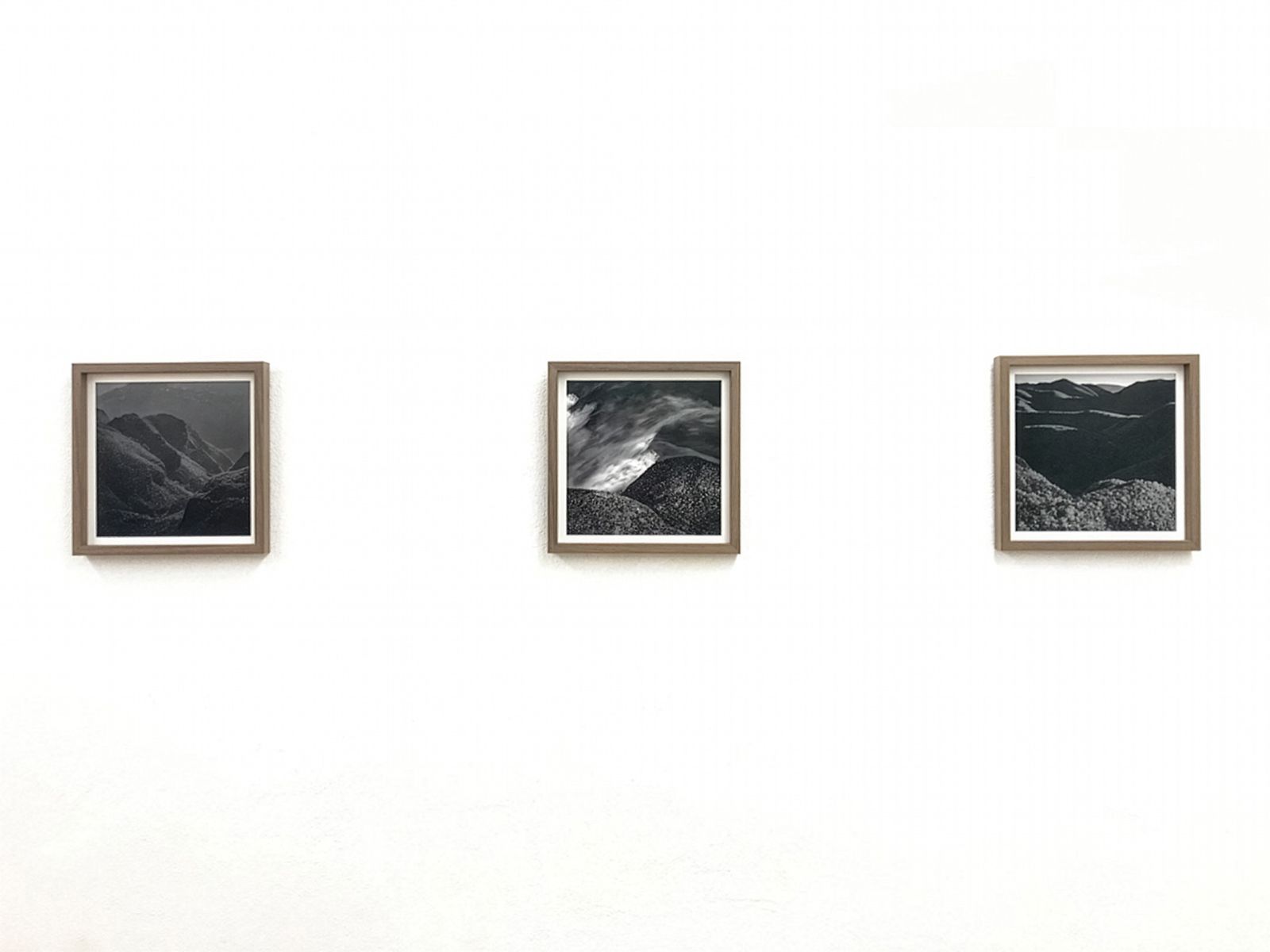 Tres fotografías enmarcadas en blanco y negro de paisajes de montaña expuestas en una pared blanca en un ambiente de galería minimalista.