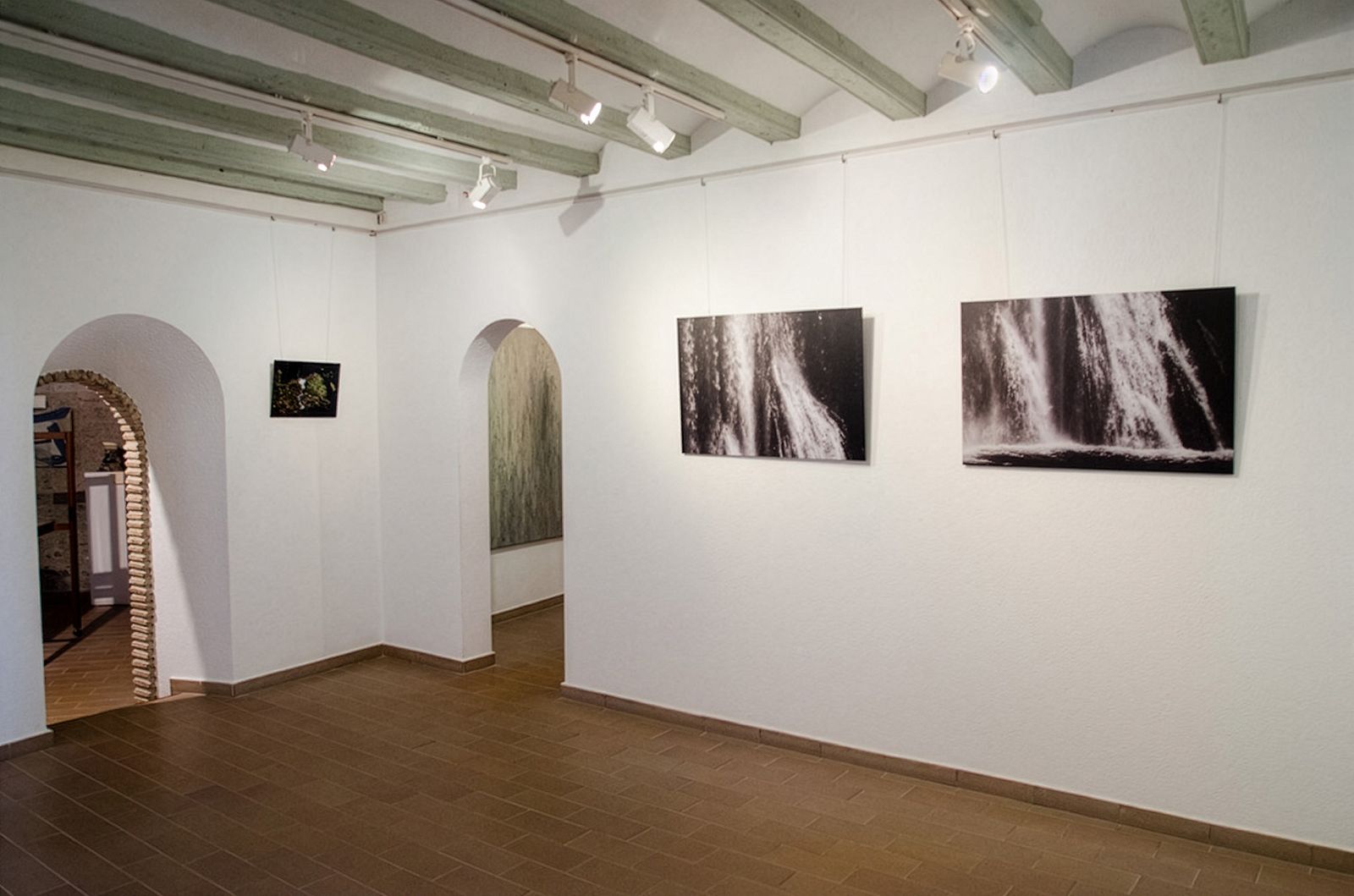 Galería con vigas de techo de madera, suelo de baldosas y fotografías de cascadas en paredes blancas.