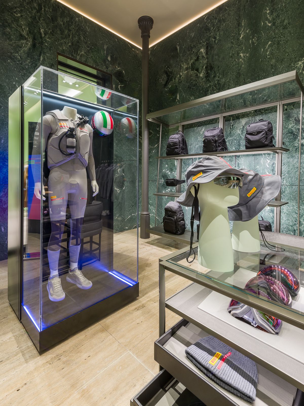 Boutique de luxe Prada amb parets de marbre verd, mostrant un maniquí amb un vestit de rendiment tancat en una vitrina de vidre.